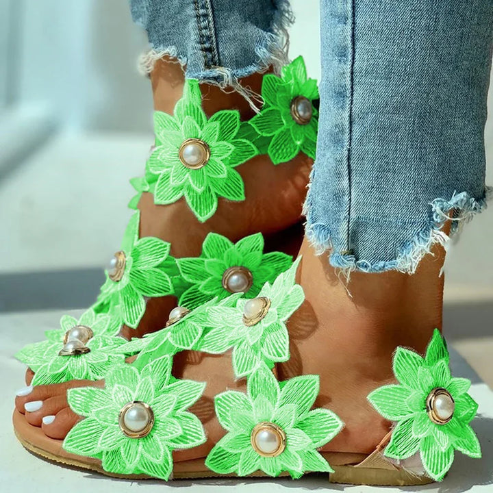 Close-up of feet wearing green floral sandals with pearl accents and frayed hem denim jeans