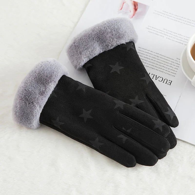 Black winter gloves with gray faux fur cuffs and star pattern on white surface with magazine and coffee