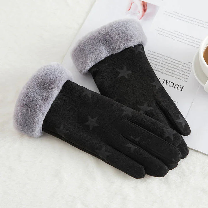 Black winter gloves with gray faux fur cuffs and star pattern on white surface with magazine and coffee