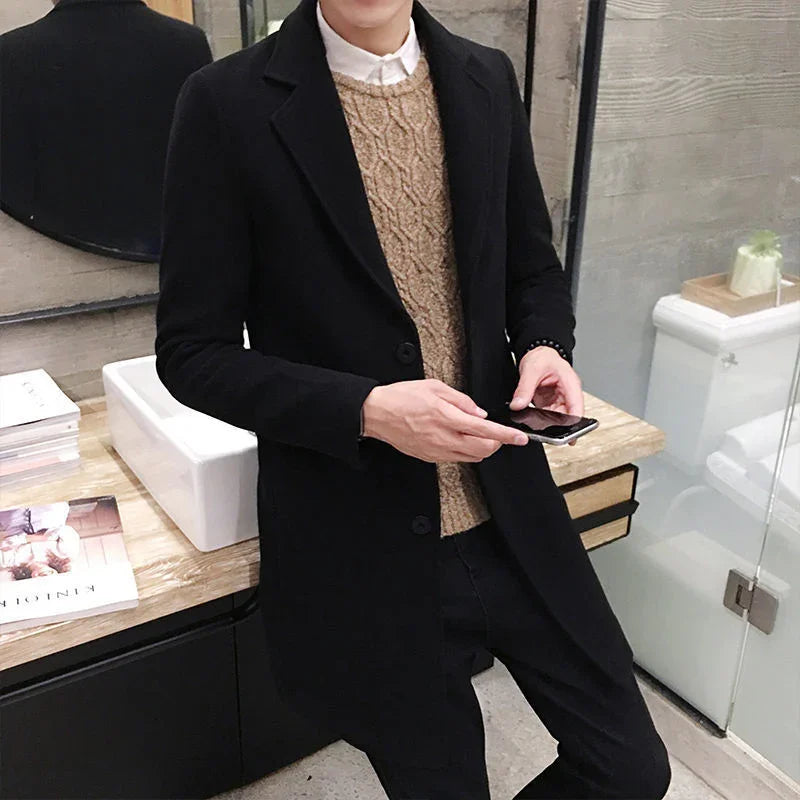 Man wearing black overcoat and brown sweater holding smartphone in modern bathroom with marble countertop