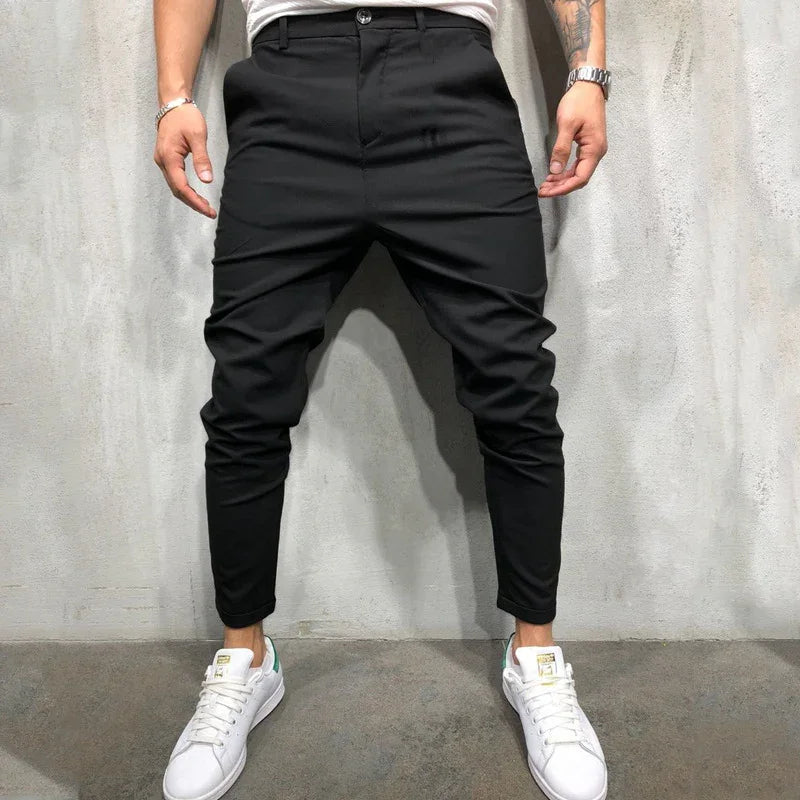 Man wearing black tapered jogger pants and white sneakers standing against gray concrete wall