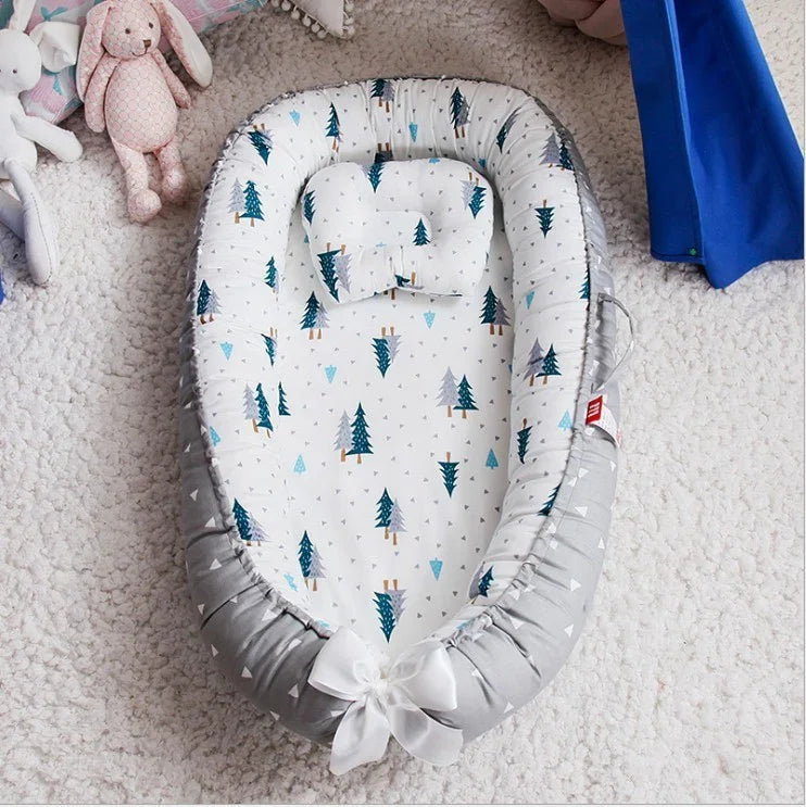 Gray and white baby nest with blue tree pattern and matching pillow on soft carpet, surrounded by plush toys