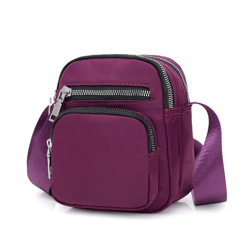 Compact purple crossbody bag with multiple zippered pockets and adjustable strap