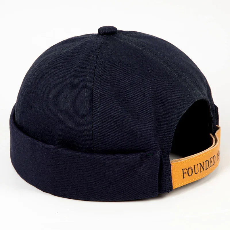 Black Docker cap with folded brim and adjustable tan leather strap reading 'FOUNDED'