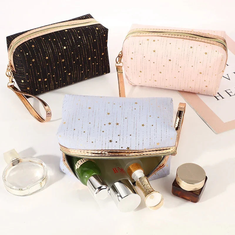 Set of three star-patterned cosmetic bags in black, pink, and light blue with gold zippers and wrist straps