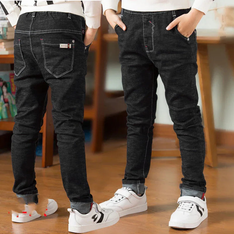 Front and back views of kids wearing black denim jeans with white sneakers indoors