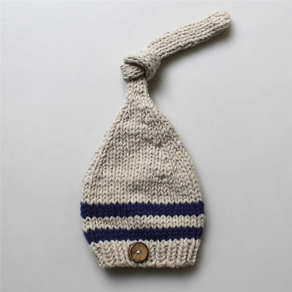 Knitted beige baby hat with blue stripes and wooden button on gray background