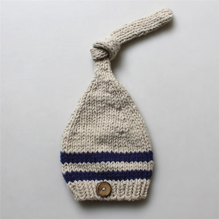Knitted beige baby hat with blue stripes and wooden button on gray background