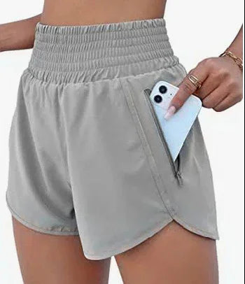 Woman wearing light gray high-waisted athletic shorts with zipper pocket holding a smartphone