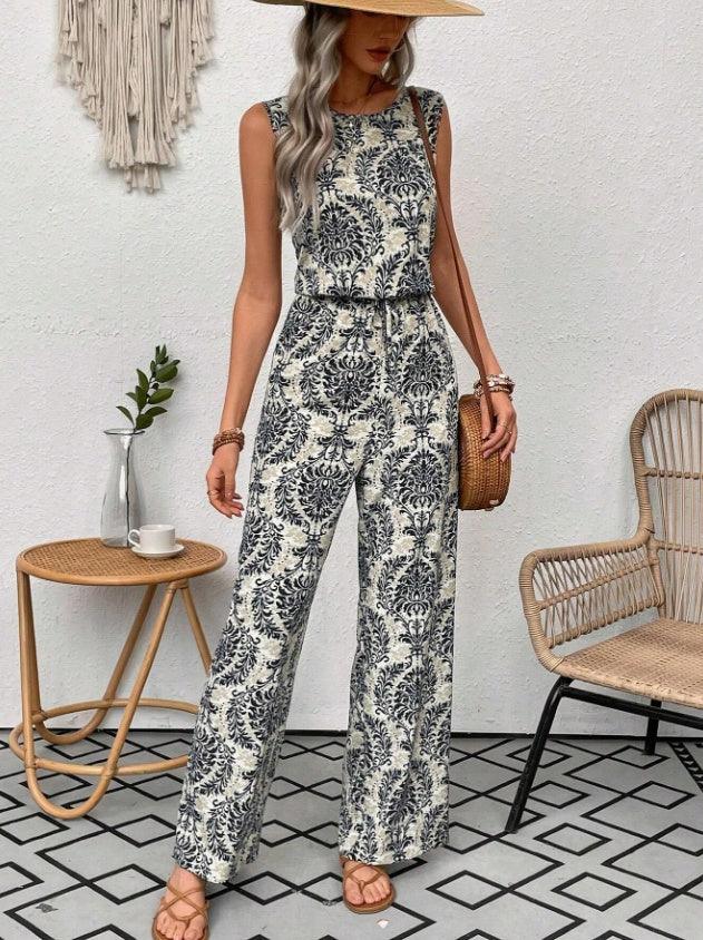 Woman in sleeveless patterned jumpsuit with wide leg pants wearing a straw hat and holding a wicker handbag