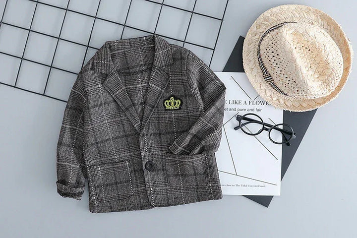 gray plaid toddler blazer with green crown patch, black glasses, straw hat, and stylish papers on gray background