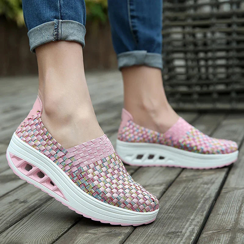 Pink multicolor woven slip-on platform shoes with thick white sole worn with rolled-up jeans on wooden deck