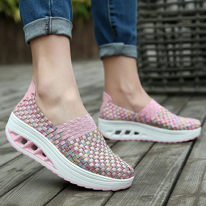 Pink multicolor woven slip-on platform shoes with thick white sole worn with rolled-up jeans on wooden deck