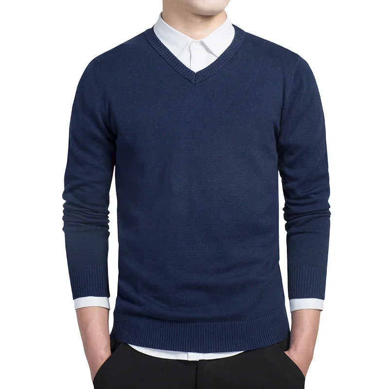 Man wearing navy blue V-neck sweater over white dress shirt with tucked hands