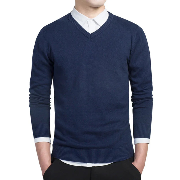 Man wearing navy blue V-neck sweater over white dress shirt with tucked hands