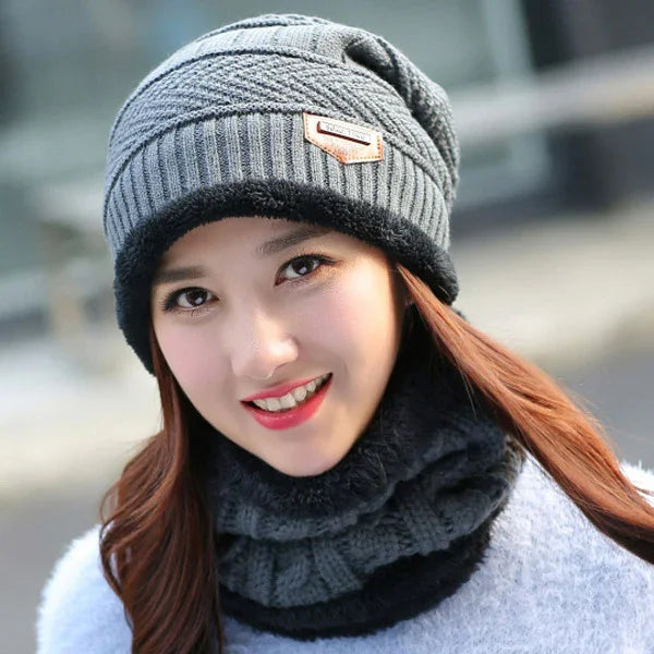 Young woman wearing a grey knit beanie and matching black-trimmed neck warmer, smiling outdoors