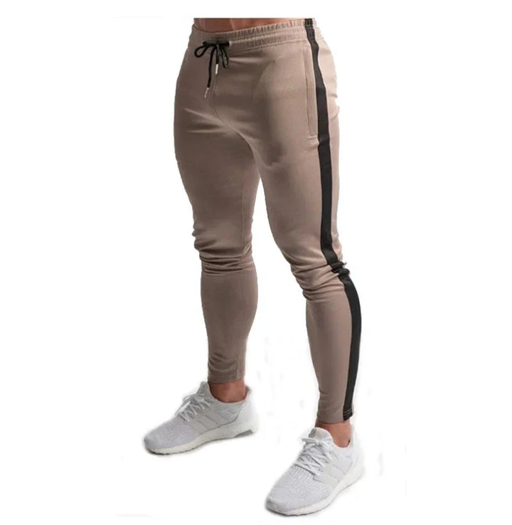 Men's slim fit beige jogger pants with black side stripe and drawstring waist, paired with white sneakers