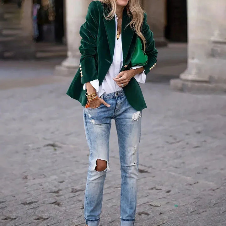Woman wearing green velvet blazer, white blouse, ripped light blue jeans, and green handbag on city street