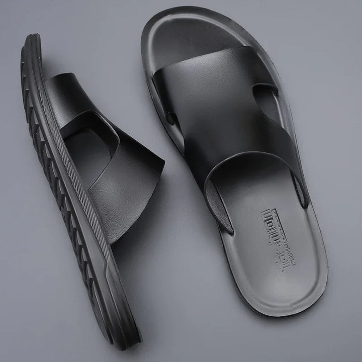 Pair of black slide sandals with textured soles on gray background