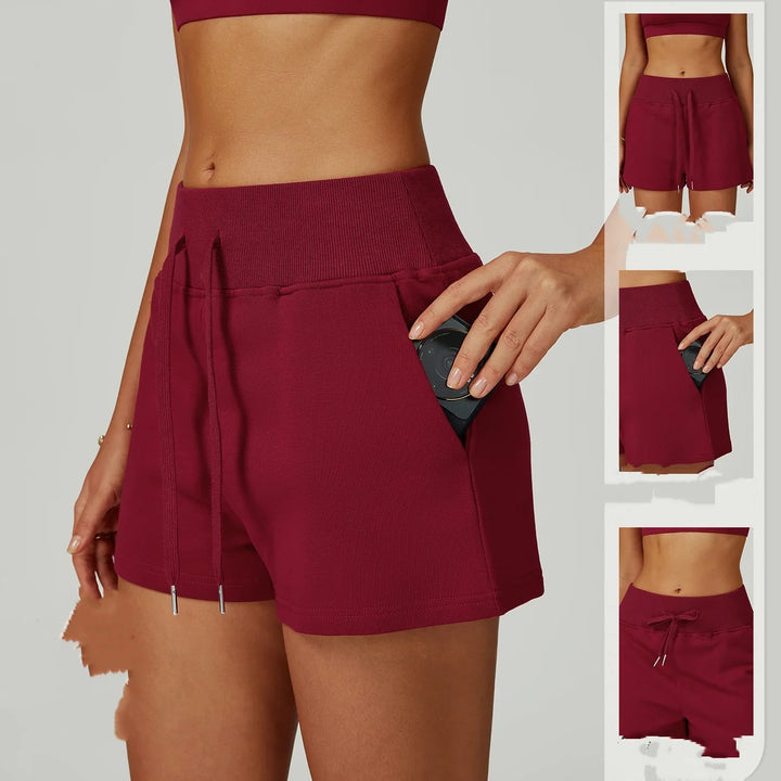 Close-up of woman wearing maroon drawstring athletic shorts with pockets, holding a black device