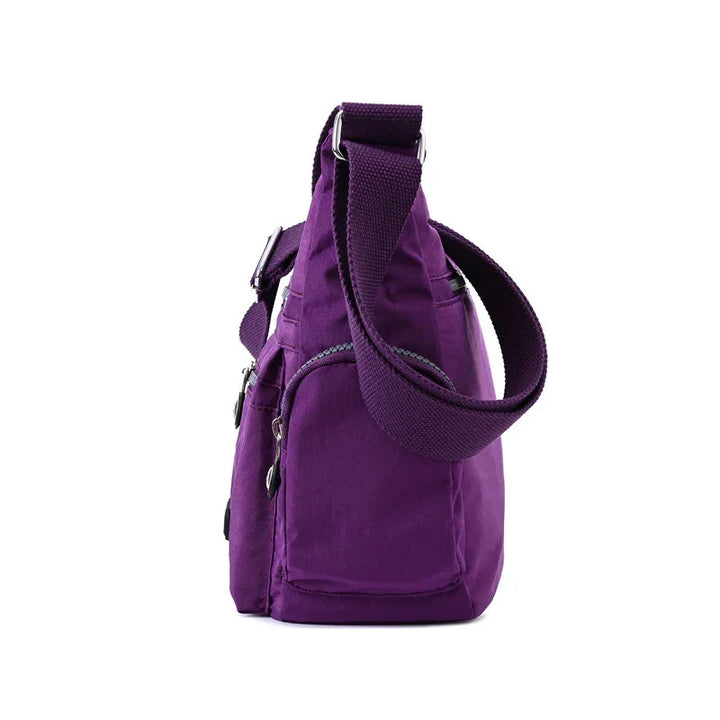 Side view of a purple canvas shoulder bag with adjustable strap and zipper pockets