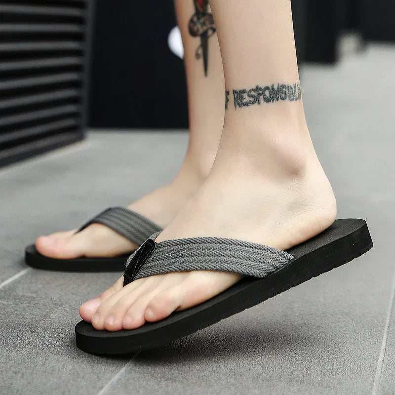 Close-up of feet wearing black and gray flip-flop sandals on gray tiled floor