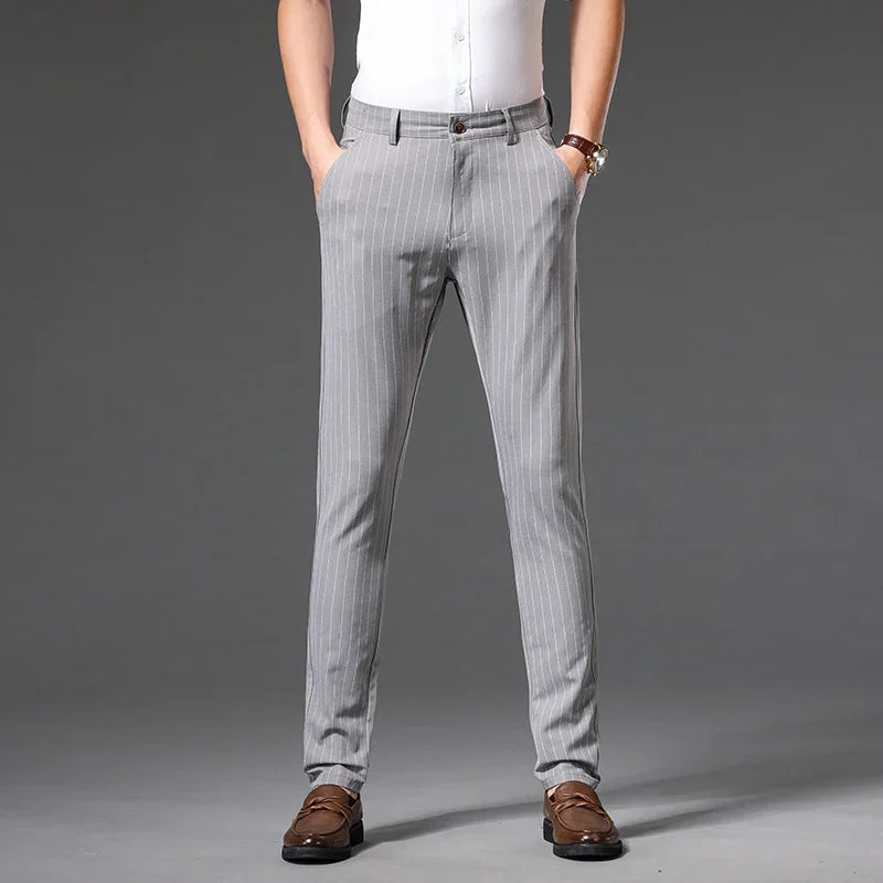 Man wearing slim-fit gray pinstripe trousers with brown loafers and white shirt on grey background