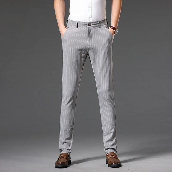 Man wearing slim-fit gray pinstripe trousers with brown loafers and white shirt on grey background