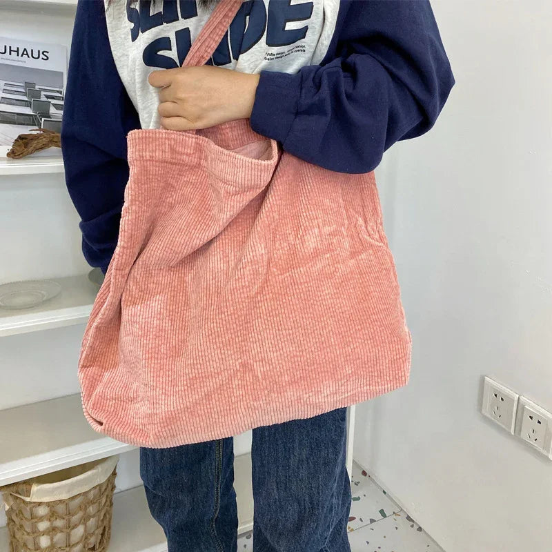 Person holding large soft pink corduroy tote bag wearing navy blue and white sweatshirt and blue jeans