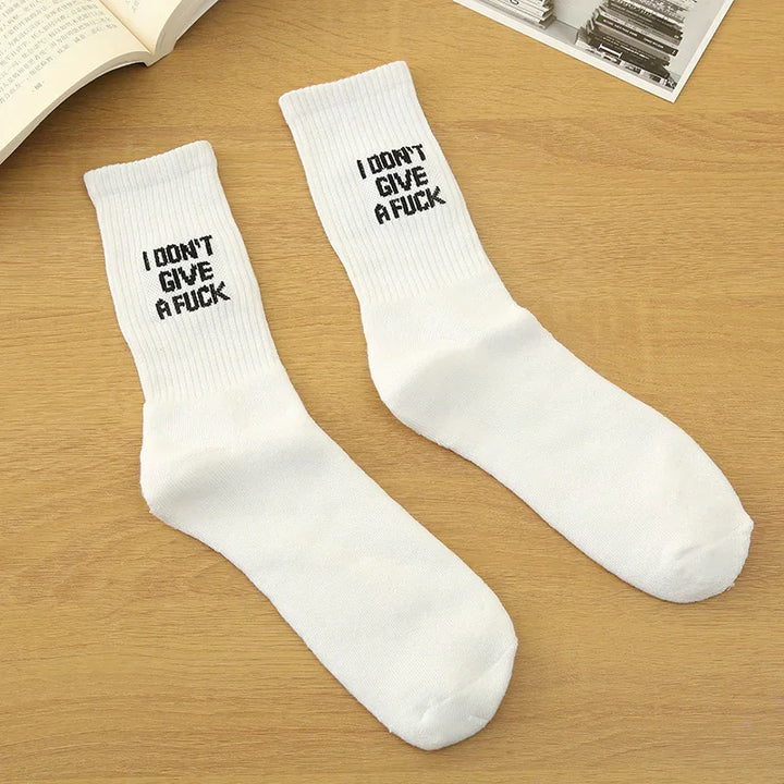 Pair of white crew socks with black text I DON'T GIVE A F**K laid on wooden surface with books