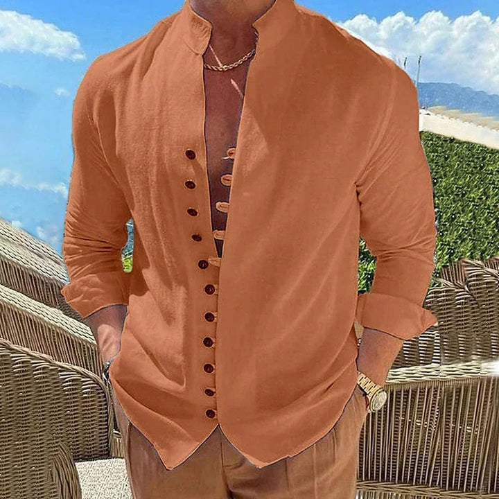 Man wearing stylish burnt orange mandarin collar shirt with rolled sleeves and brown pants outdoors