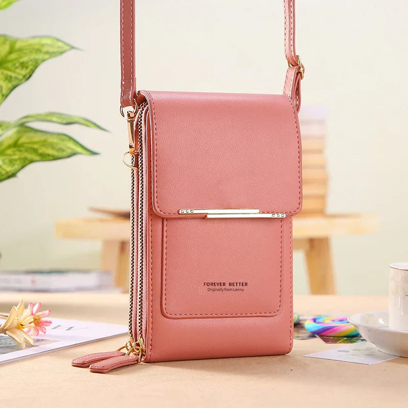 Pink faux leather crossbody bag with gold bar detail, dual zipper compartments, and adjustable strap on table