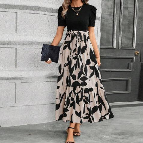 woman wearing black top and beige maxi skirt with black leaf print holding black clutch