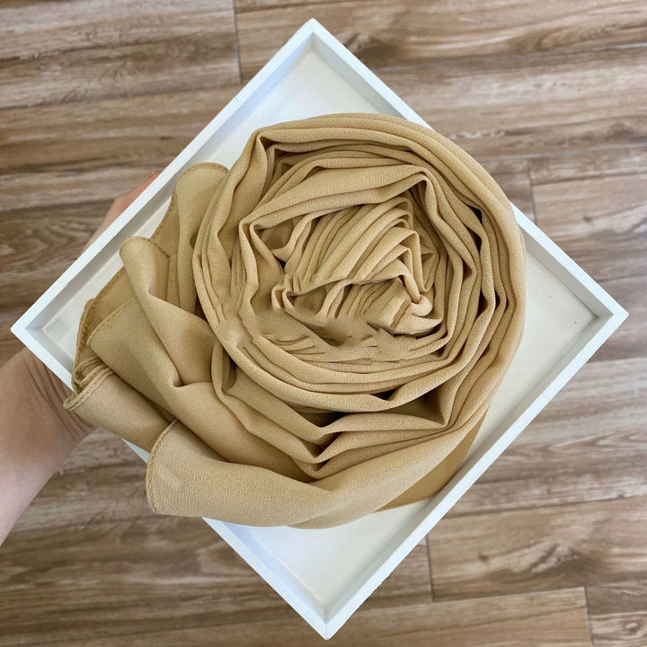 Hand holding a white tray with neatly rolled beige chiffon fabric on wooden floor background