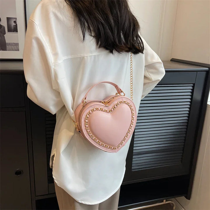 Woman wearing white shirt with stylish pink heart-shaped handbag featuring gold chain details