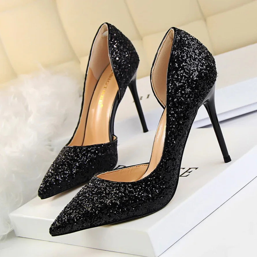 Pair of black glitter high heel stiletto shoes on white box with beige background