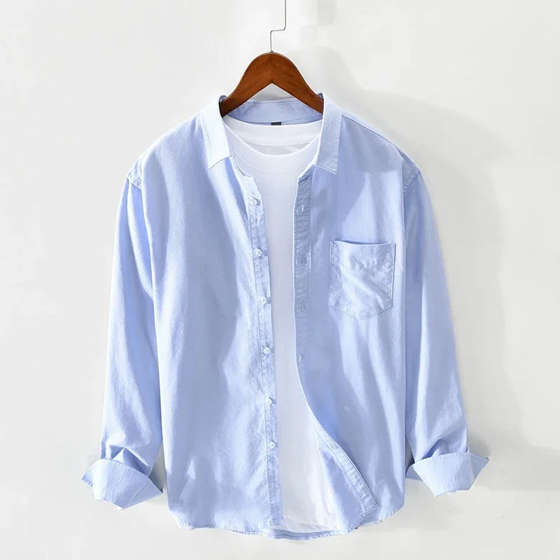 Light blue button-up shirt layered over white t-shirt on wooden hanger against white background