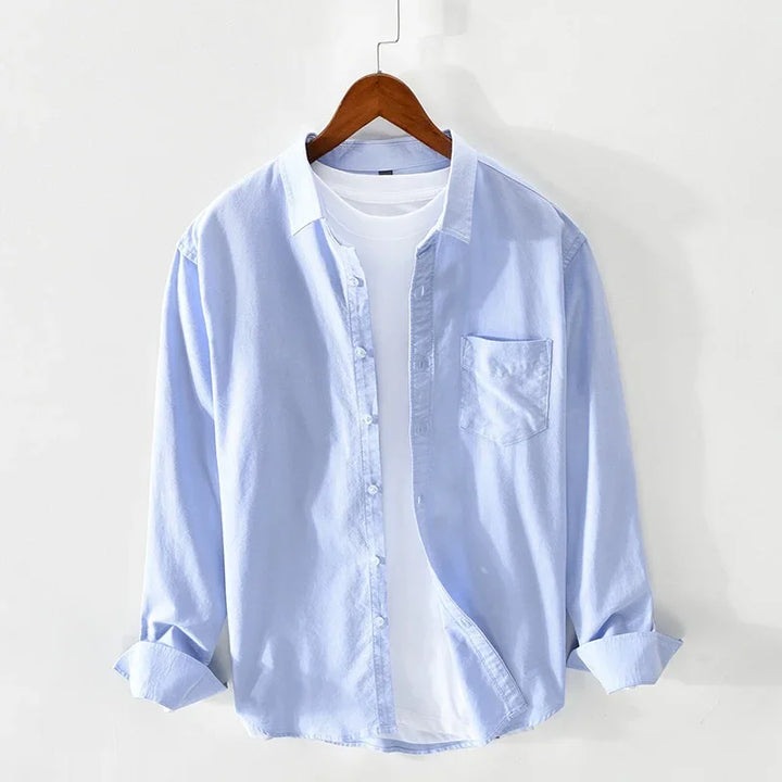 Light blue button-up shirt layered over white t-shirt on wooden hanger against white background