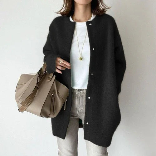 Woman wearing oversized black fuzzy cardigan, white t-shirt, gray pants, holding beige handbag