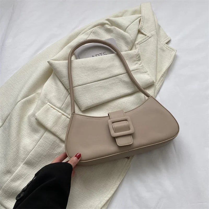 Beige leather shoulder bag with buckle detail held over cream textured blazer on white background