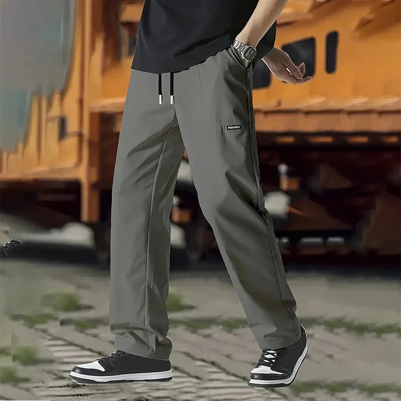 Person wearing gray casual pants with PROGRESS label and black sneakers outdoors on pavement
