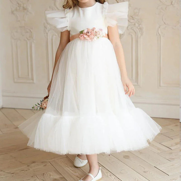 Girl wearing white tulle dress with floral belt and ruffled sleeves in elegant room