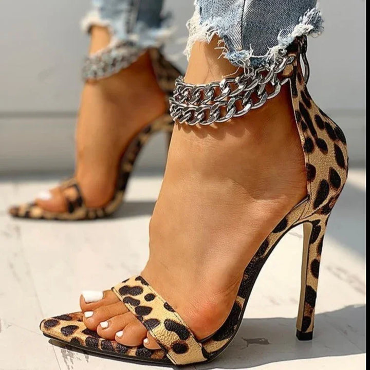 Close-up of feet wearing leopard print high heel sandals with silver chain ankle straps and distressed denim jeans
