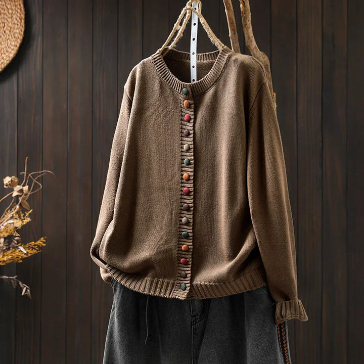 Brown knitted cardigan with colorful buttons on hangers against dark wood wall background