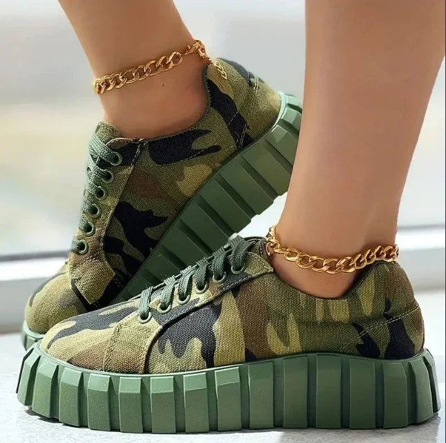 Green camo print platform sneakers with chunky soles and gold chain anklets on model's feet