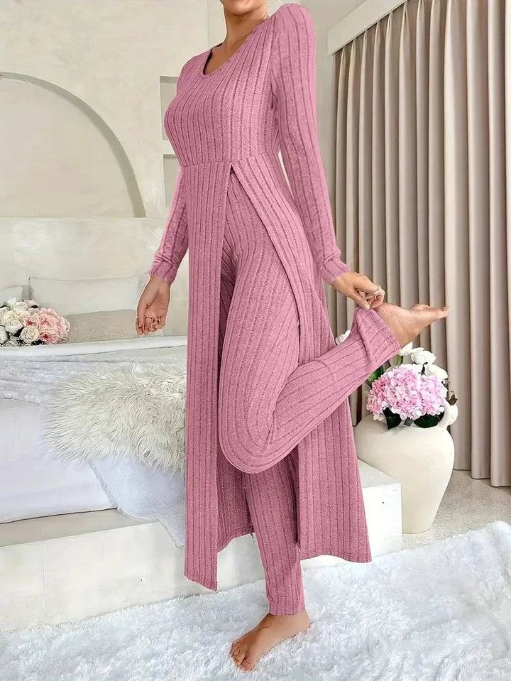 Woman in pink ribbed knit long cardigan and matching leggings posing barefoot in cozy modern bedroom
