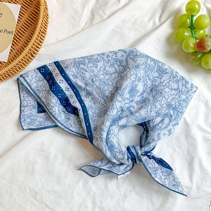 Blue and white floral patterned silk scarf with navy border on white fabric, wicker basket, and green grapes