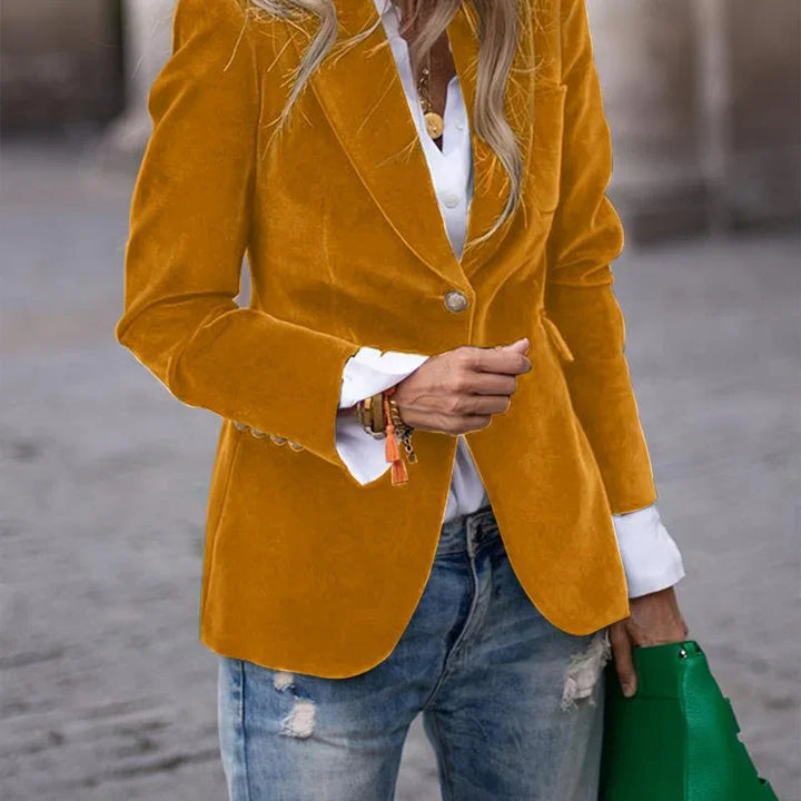Woman wearing mustard yellow velvet blazer with white shirt and ripped jeans holding green handbag