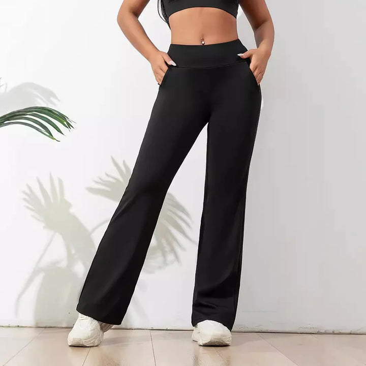 Woman wearing black wide-leg lounge pants with pockets and white sneakers against white wall