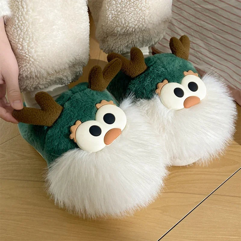 Green plush slippers with white fluffy toes and cute reindeer faces with antlers on wooden floor